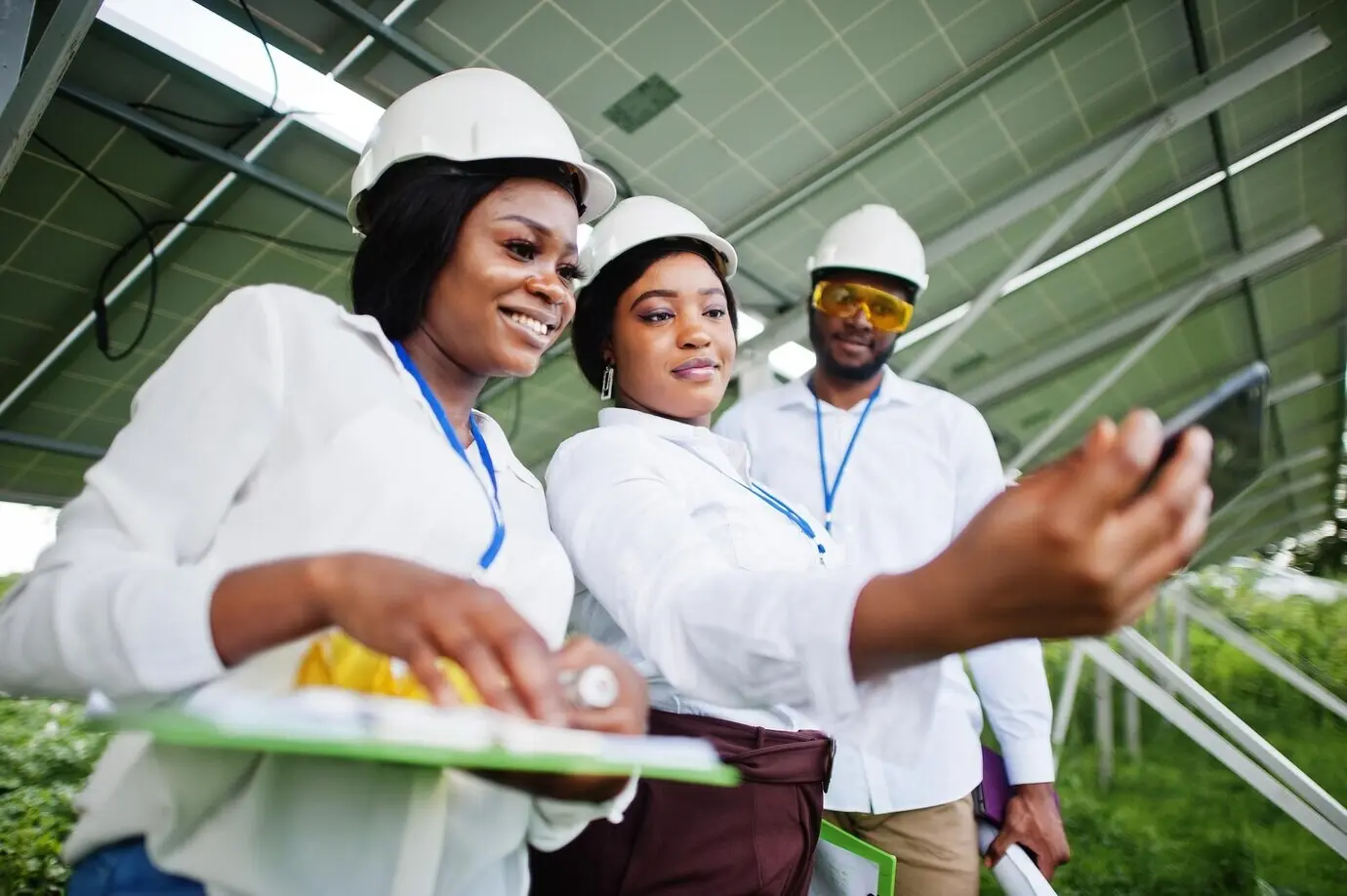 An African American technician checks the maintenance of solar panels; a group of three Black engineers meets at a solar station and takes a selfie with a phone.